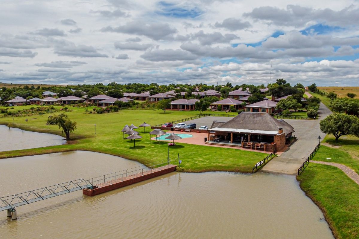 Aerial view of a residential estate featuring a clubhouse, swimming pool, and a jetty extending into a large dam.