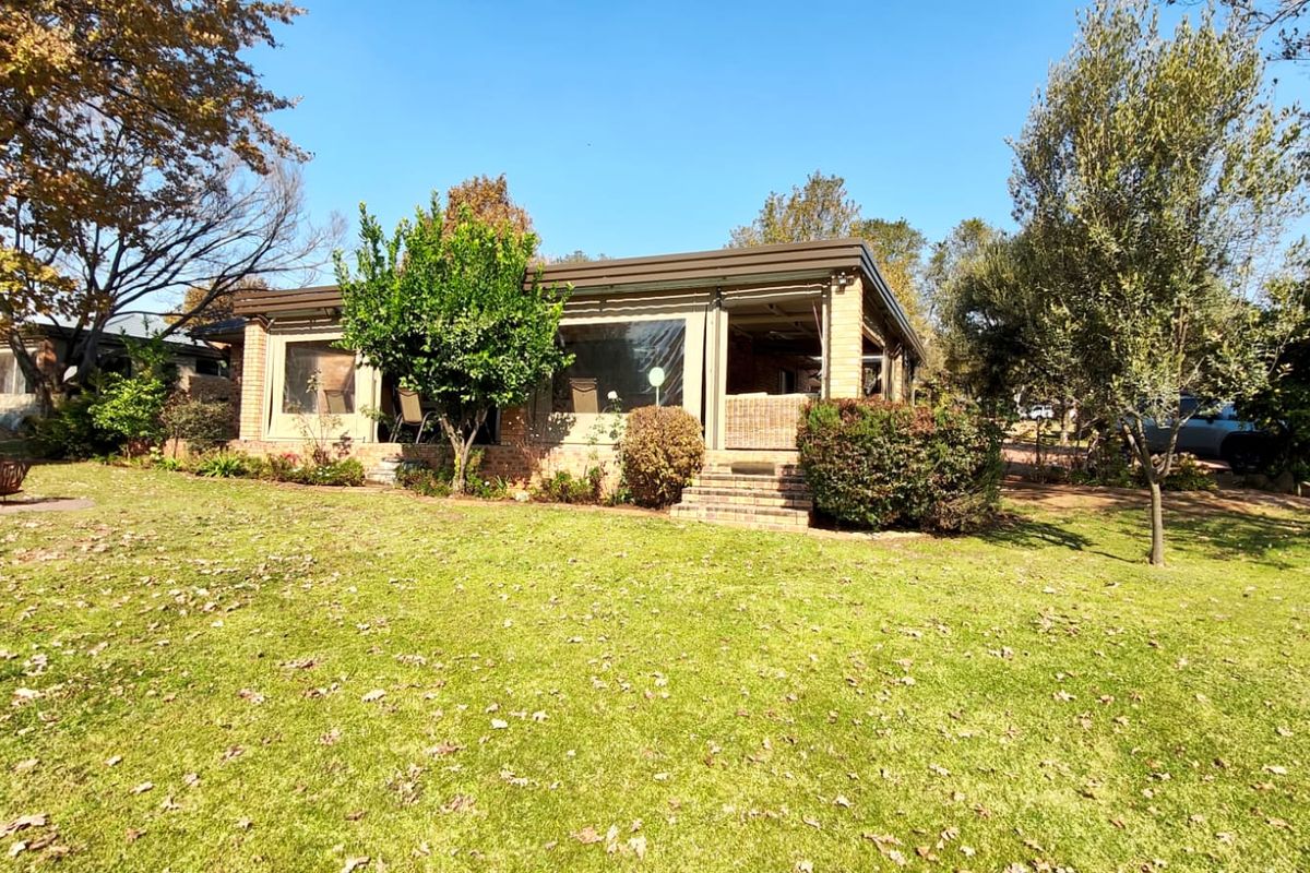 A view of the rear of the house featuring a spacious lawn, landscaped garden, and a covered patio area with protective outdoor blinds.