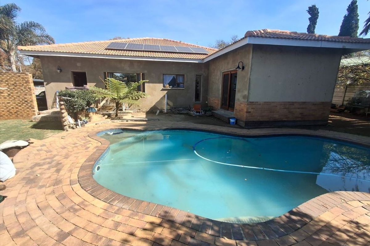 Rear exterior view featuring a swimming pool, brick paved surround, and a house with a tiled roof and installed solar panels.