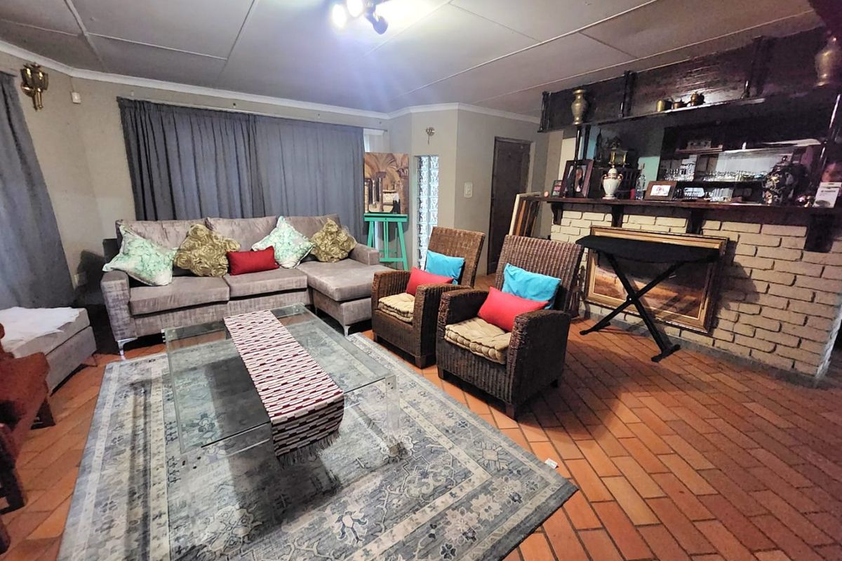 Spacious living room featuring terracotta tile flooring, a built-in brick bar area, and a coved ceiling, offering a traditional layout with potential for modernization.