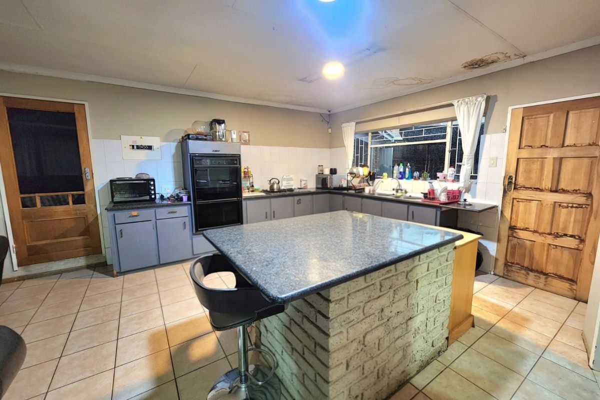 A functional kitchen featuring a central brick-based island, built-in oven, and tiled finishes, currently showing signs of ceiling water damage and general wear.