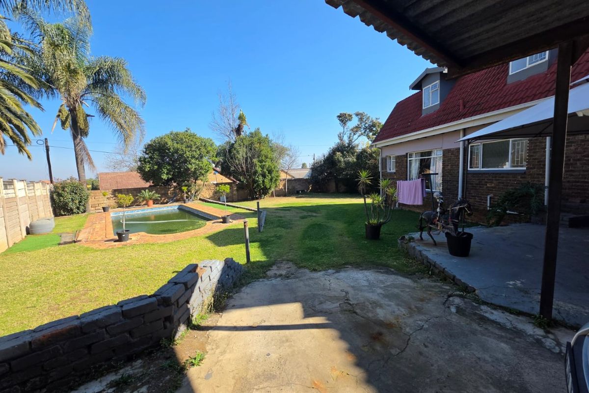Rear exterior view featuring a swimming pool, lawn area, and a covered patio attached to the main house structure.