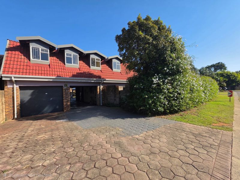 Front elevation of a house featuring a tiled roof, dormer windows, a garage, and a paved driveway.