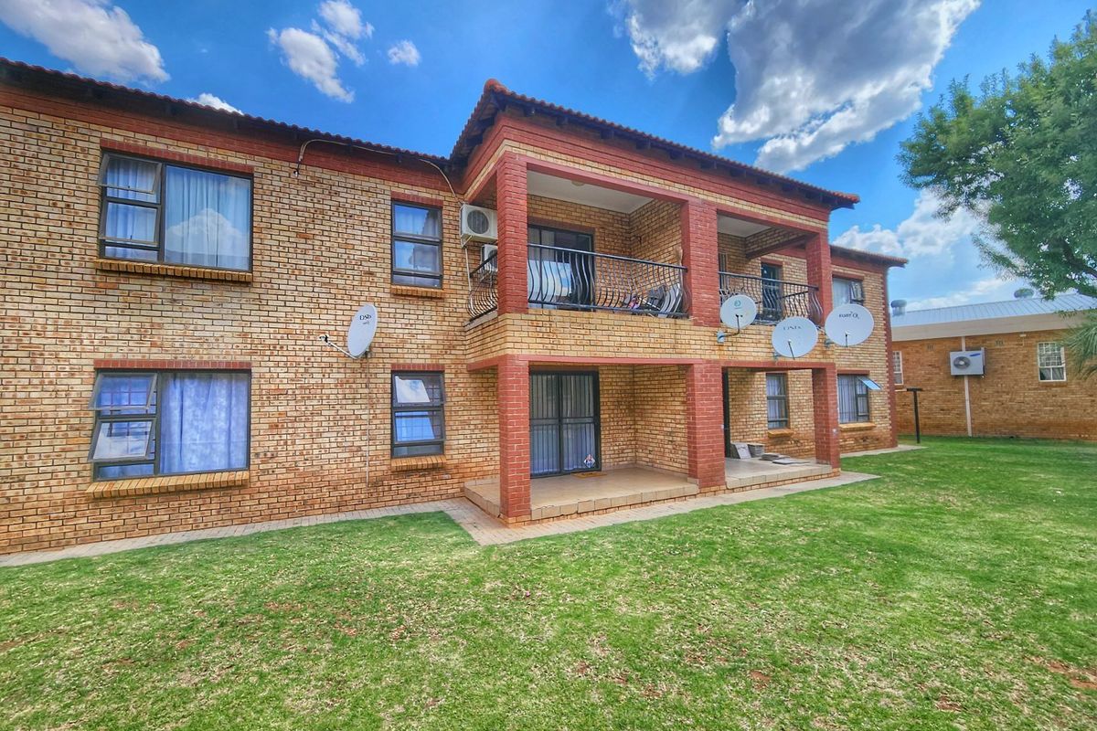 Rear view of a multi-story face brick apartment building featuring balconies, patios, and established lawn area.