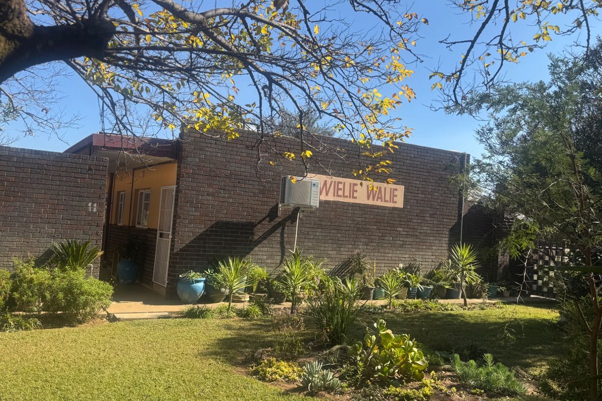 A view of the rear exterior of the apartment building featuring a brick facade, established garden, and an external air conditioning unit.