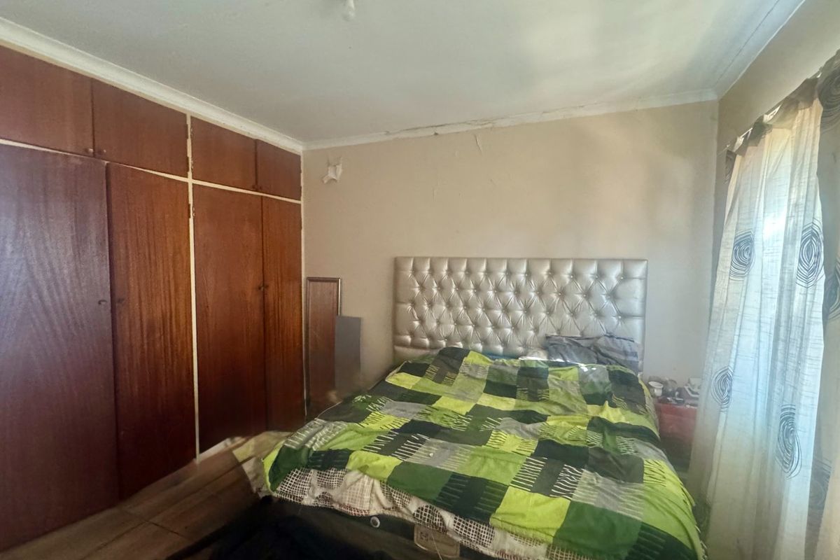 A bedroom featuring built-in wooden cupboards, tiled flooring, and coved ceilings, currently requiring cosmetic updates to the wall and ceiling finishes.