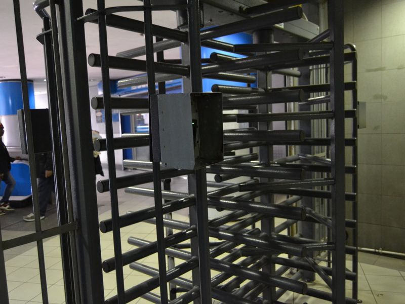 A security turnstile entry point featuring an access control reader with exposed wiring and tiled flooring.