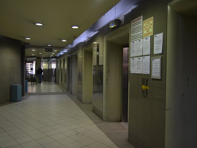 A communal apartment building hallway featuring elevator access, tiled flooring, and mirrored wall panels with posted building notices.