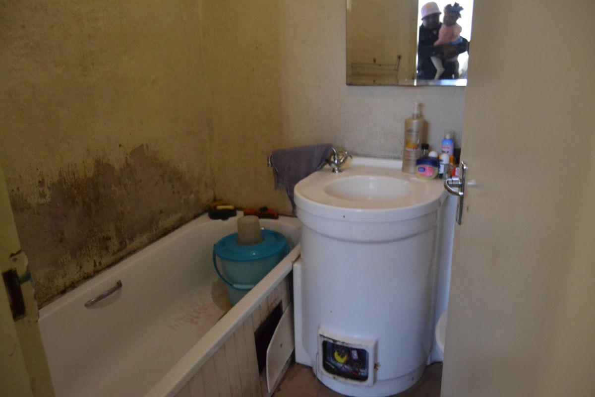 A small bathroom featuring a bathtub and pedestal basin, currently requiring significant renovation due to visible wall surface damage and deterioration.
