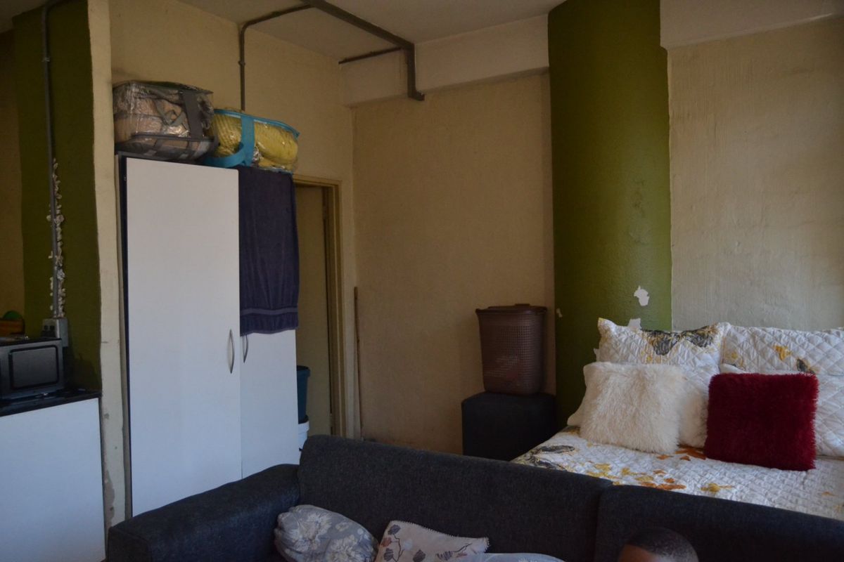 A bedroom featuring a built-in wardrobe and exposed ceiling piping, with visible wear on the painted column.