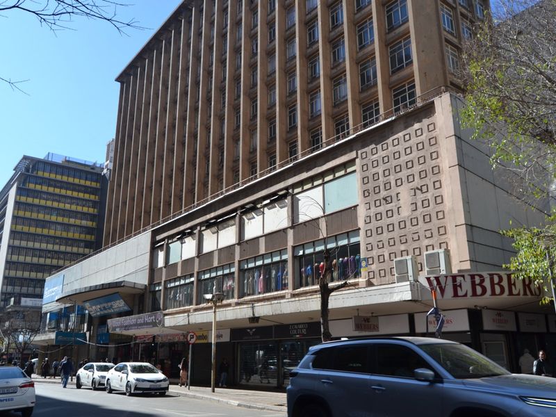 Street-level view of a multi-story apartment building featuring commercial storefronts on the ground floor and a weathered concrete facade.