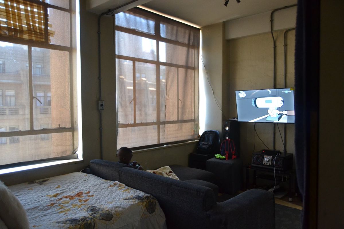 Living area featuring large industrial-style windows, exposed electrical conduit, and concrete ceiling beams, offering a unique urban aesthetic with potential for modernization.
