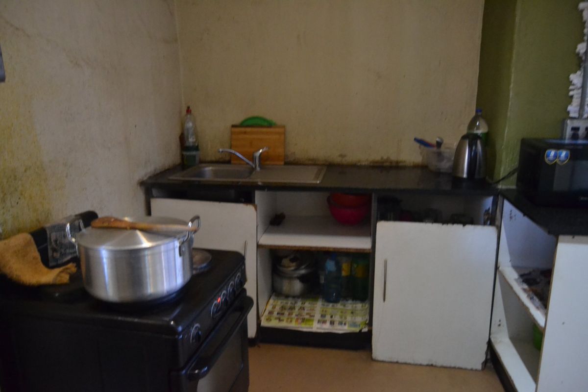 A compact kitchen area featuring a stainless steel sink, stone countertop, and freestanding stove, currently showing significant wear and requiring cosmetic updates.