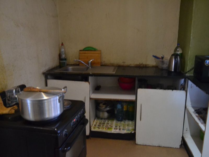 A compact kitchen area featuring a stainless steel sink, stone countertop, and freestanding stove, currently showing significant wear and requiring cosmetic updates.