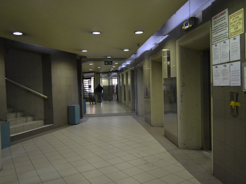 A communal apartment building hallway featuring tiled flooring, recessed lighting, an elevator bank, and access to a staircase.