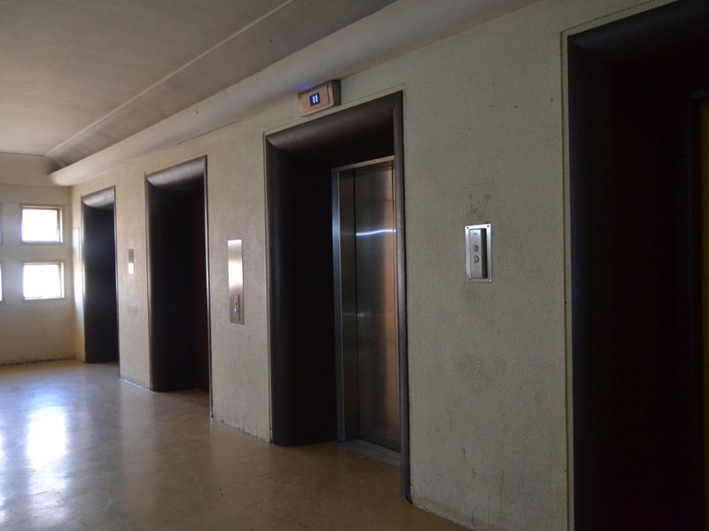 A communal apartment hallway featuring multiple elevator access points with stainless steel doors and call panels.