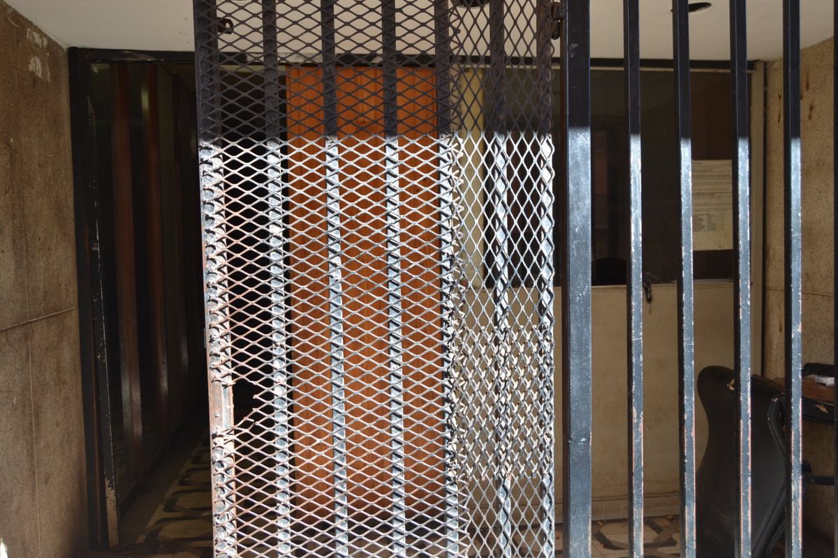 Entrance area featuring a heavy-duty metal security gate and bars, showing significant signs of wear and corrosion.