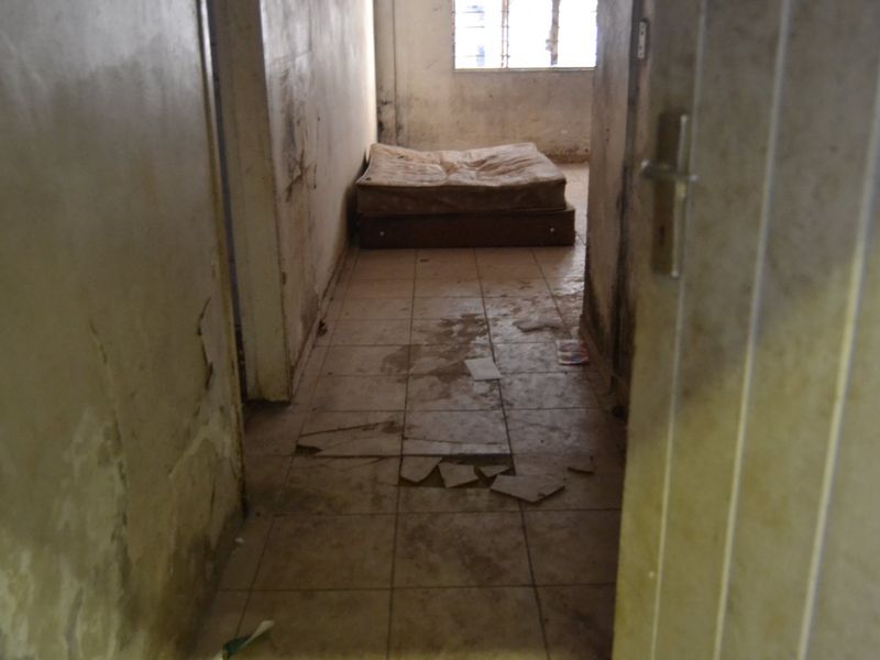 A bedroom in poor condition featuring damaged floor tiles and significant wall deterioration, requiring extensive renovation and repair.