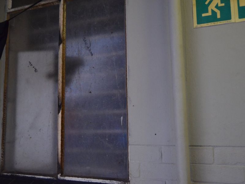 A dimly lit hallway area featuring a louvered window and an emergency exit sign on the wall.