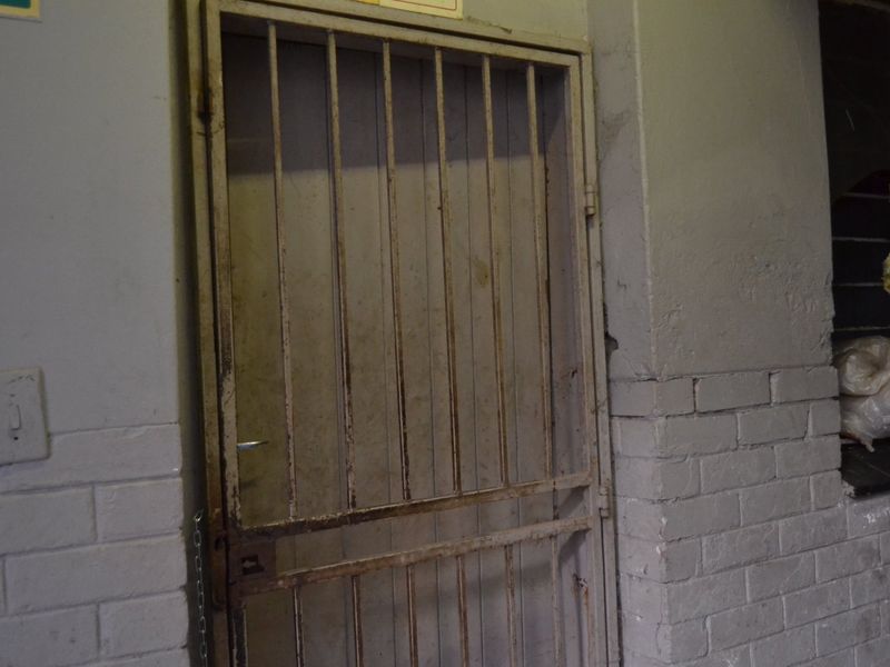 A secure metal gate entrance featuring painted brickwork walls, showing signs of wear and corrosion.