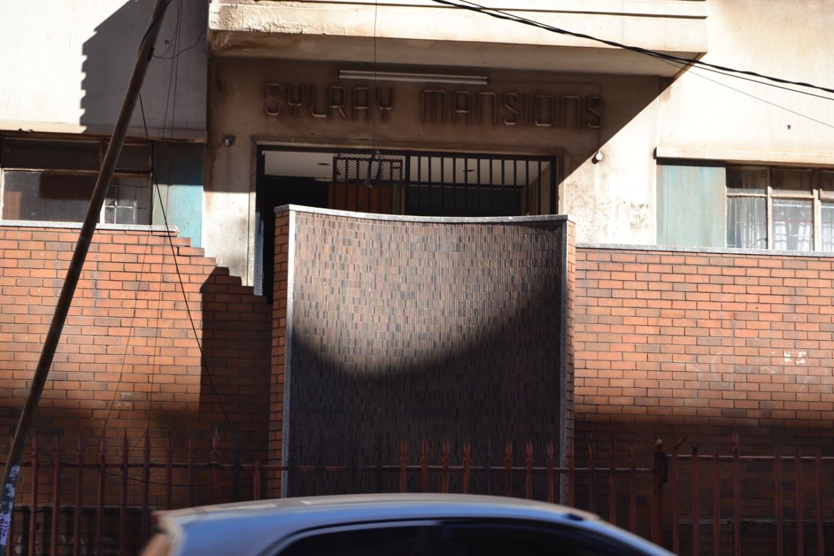 Front entrance view of Sylray Mansions featuring a brick boundary wall, security gate, and building signage.