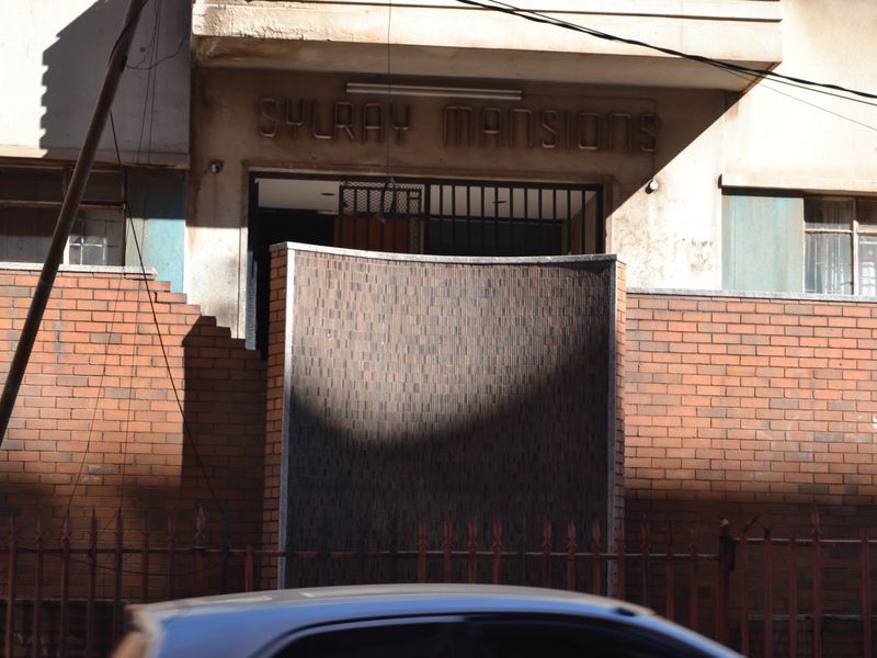 Front entrance view of Sylray Mansions featuring a brick boundary wall, security gate, and building signage.