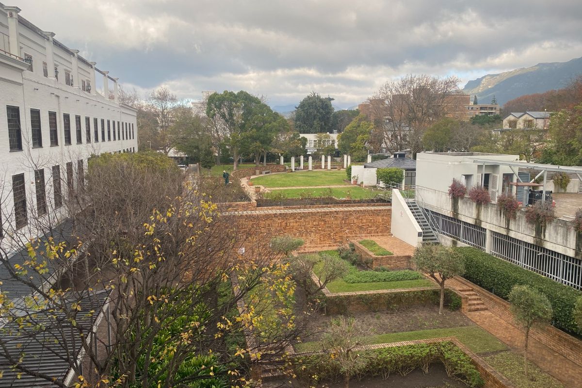Elevated view of a commercial property rear courtyard featuring tiered brick retaining walls, landscaped garden beds, and paved walkways between building wings.