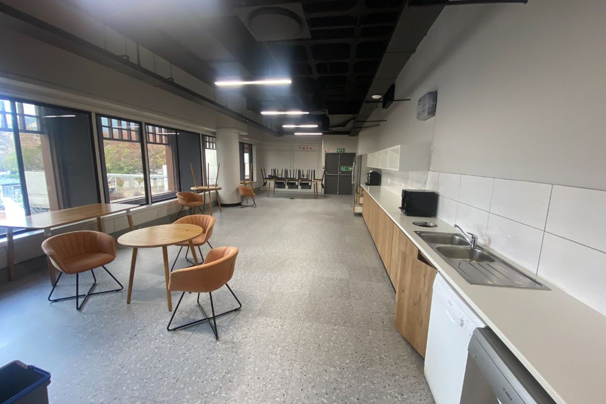 A spacious commercial kitchen area featuring modern cabinetry, a stainless steel sink, tiled backsplash, and large windows providing ample natural light.
