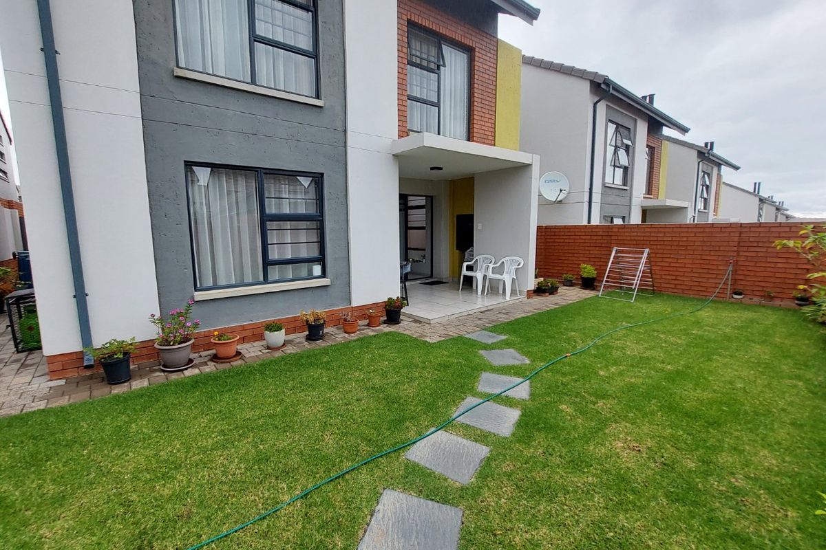 Rear view of the townhouse featuring a private garden with a paved patio, stone pathway, and brick boundary wall.
