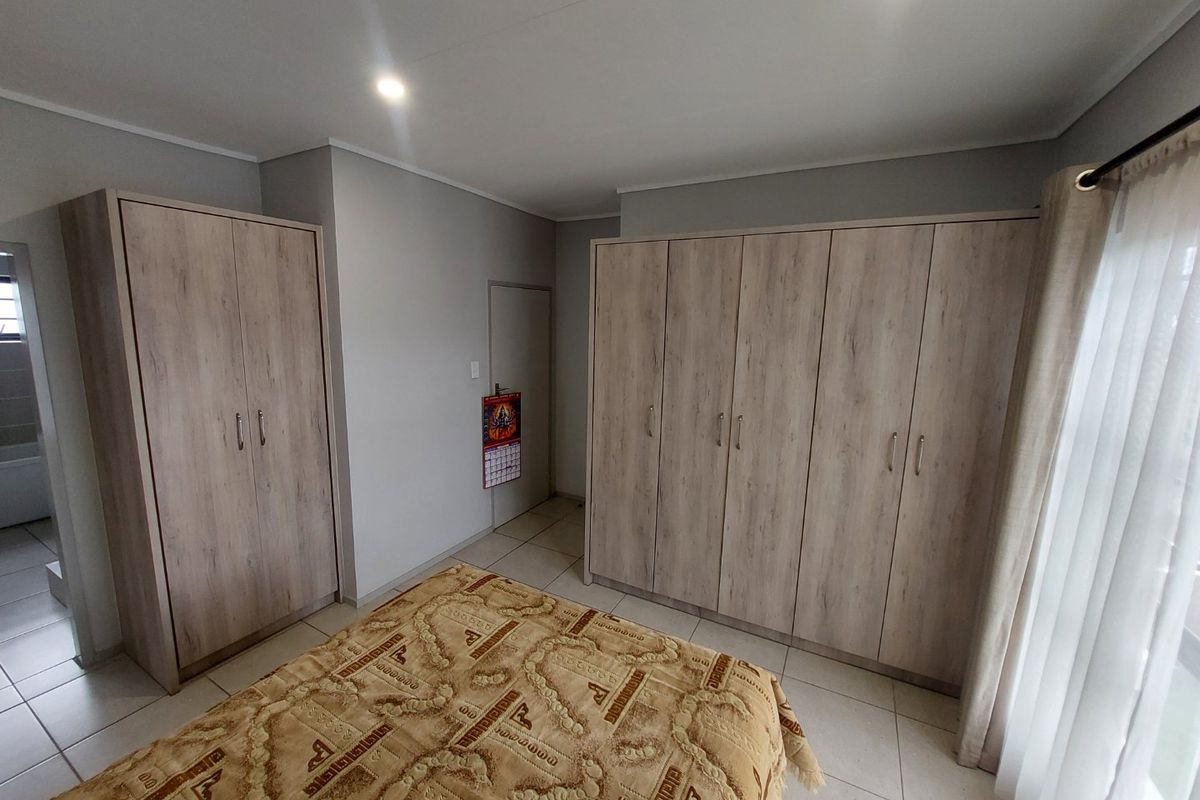 A well-maintained bedroom featuring extensive built-in wooden cupboards, neutral tiled flooring, and modern recessed lighting.