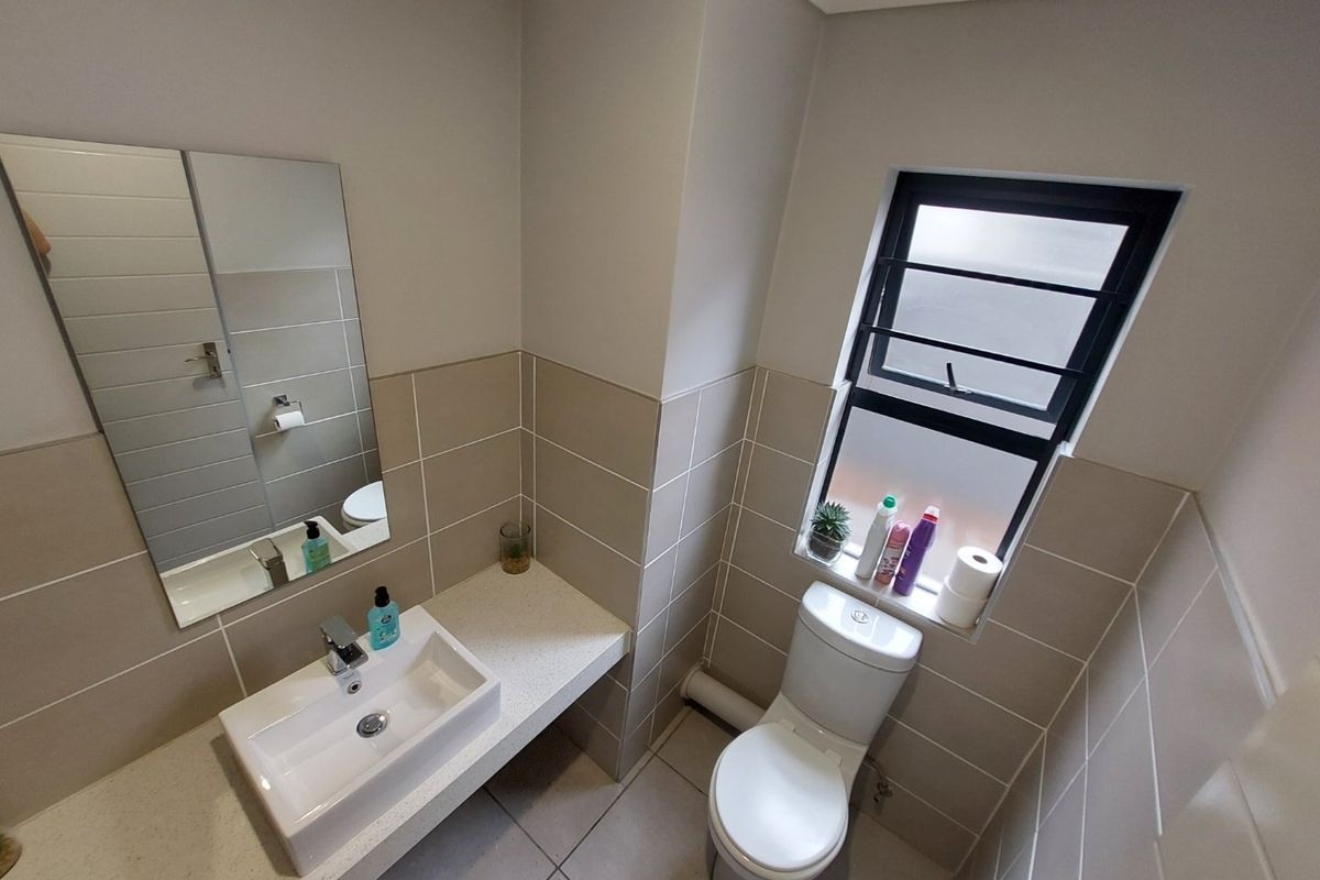 A clean and modern bathroom featuring a wall-mounted basin, tiled splashbacks, tiled flooring, and a window with security bars.