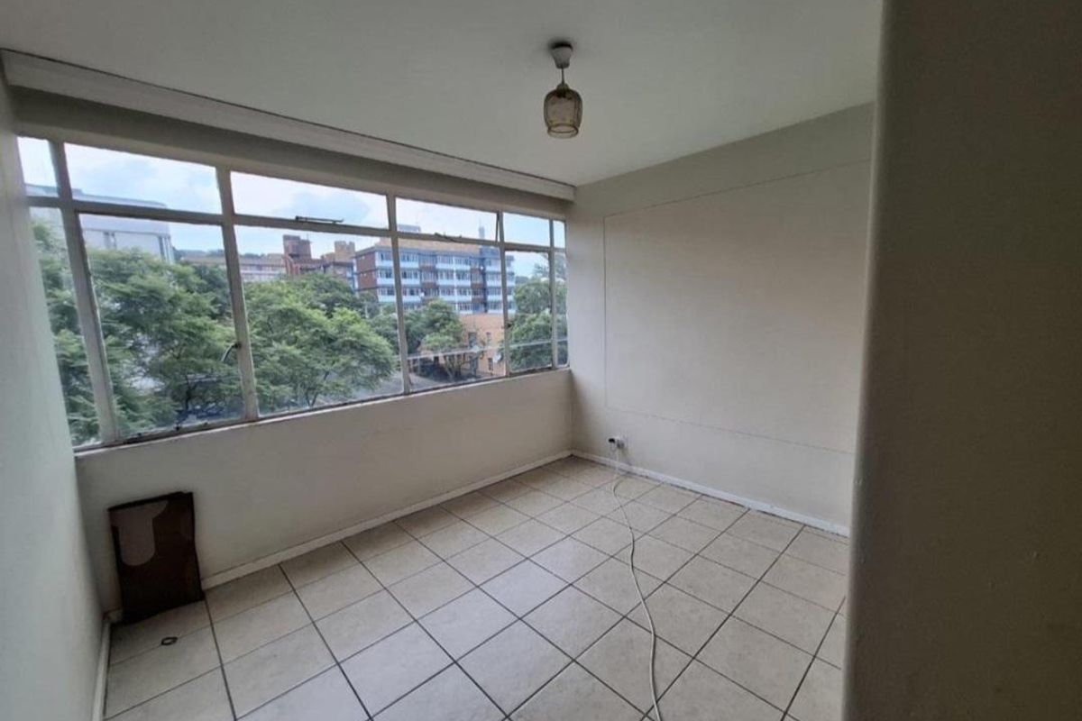 An empty, sunlit living area featuring tiled flooring and large windows with an urban view, ready for personalization.