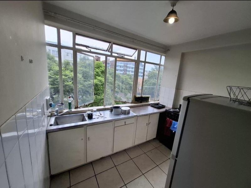 A functional kitchen featuring tiled flooring, a stainless steel sink, and large windows providing natural light and an urban view.