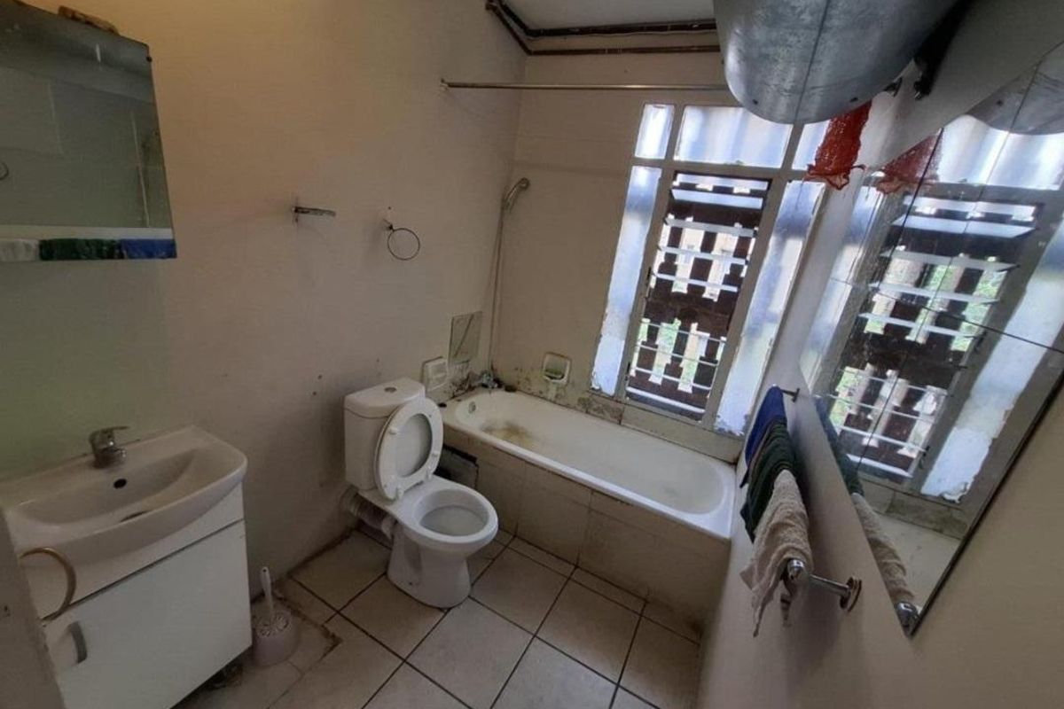A dated bathroom featuring a vanity, toilet, and bathtub, requiring significant renovation and cosmetic updates to improve its overall condition and functionality.