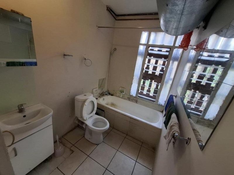 A dated bathroom featuring a vanity, toilet, and bathtub, requiring significant renovation and cosmetic updates to improve its overall condition and functionality.