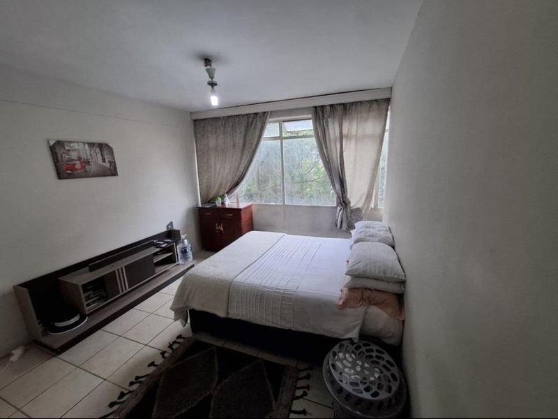 A functional bedroom featuring tiled flooring and a large window that provides natural light.