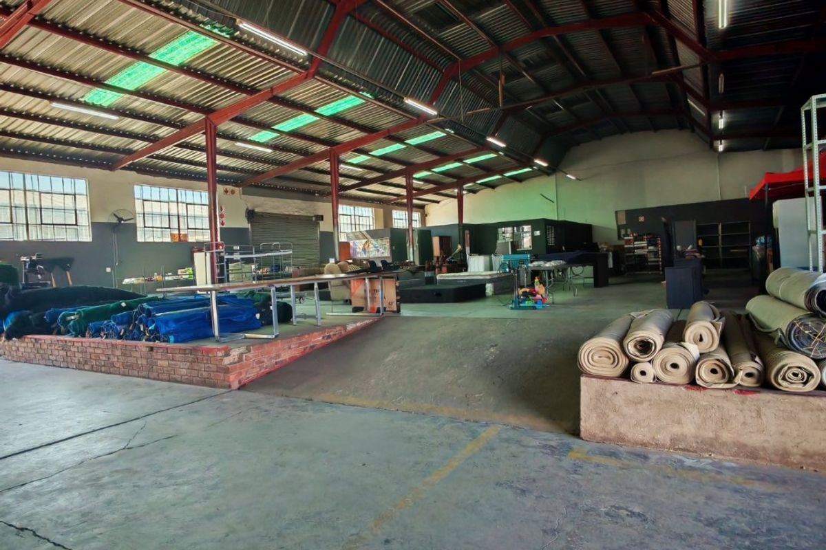 Spacious industrial warehouse featuring exposed steel roof trusses, concrete flooring, and a built-in brick loading platform with an access ramp.