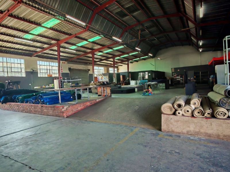 Spacious industrial warehouse featuring exposed steel roof trusses, concrete flooring, and a built-in brick loading platform with an access ramp.