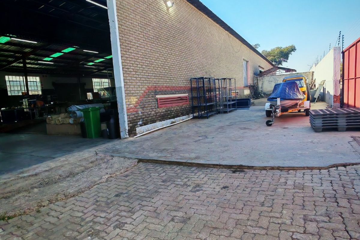 Exterior view of an industrial property featuring a brick facade, concrete apron, and paved driveway area with access to the main warehouse space.