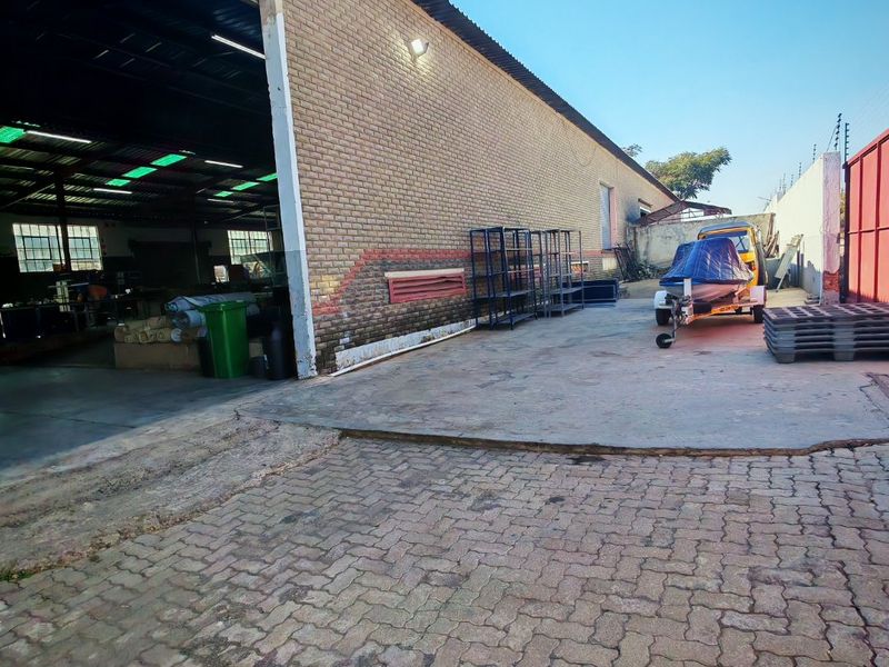 Exterior view of an industrial property featuring a brick facade, concrete apron, and paved driveway area with access to the main warehouse space.