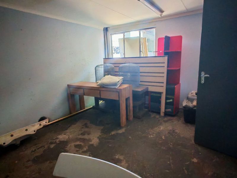 A utility space featuring concrete flooring, a casement window, and basic lighting, currently used for storage and requiring cosmetic refurbishment.