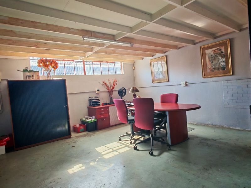 Industrial-style office space featuring exposed timber ceiling beams, high-level windows, and a painted concrete floor, suitable for a functional workspace.