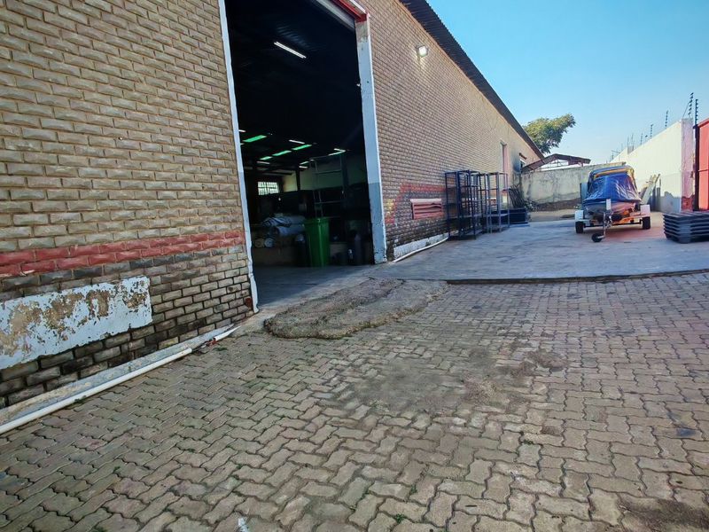 Rear industrial exterior featuring a large roller door access point, brick facade, and paved yard area with perimeter electric fencing.