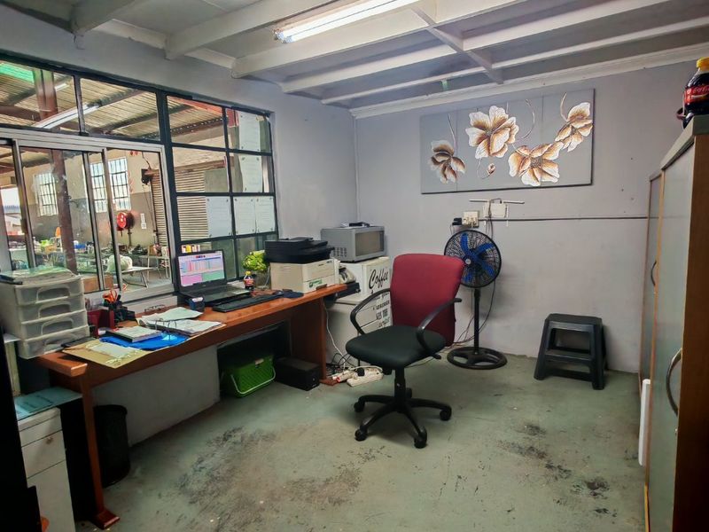 Functional industrial office space featuring exposed beam ceilings, large steel-framed windows overlooking the warehouse, and durable painted concrete flooring.
