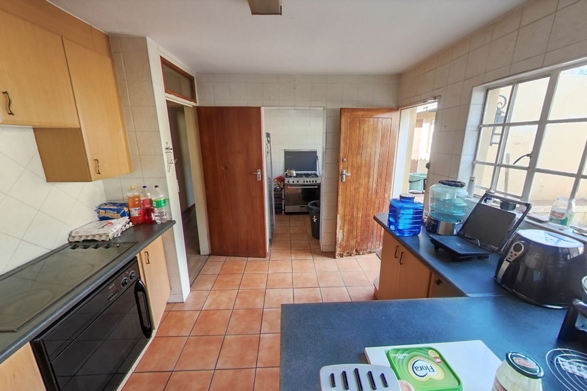 A functional kitchen featuring built-in cabinetry, tiled flooring, and a tiled backsplash, with an adjacent scullery area visible through the doorway.