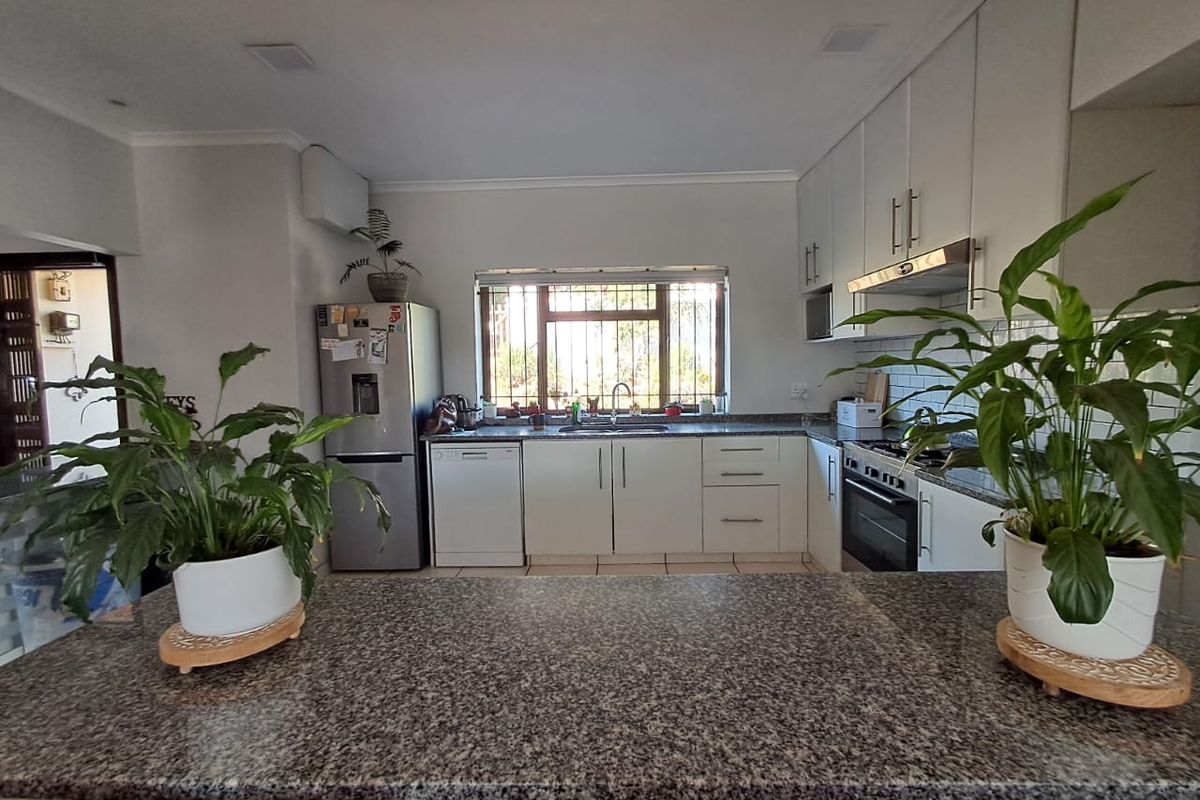 A functional kitchen featuring granite countertops, white cabinetry, a built-in oven with extractor fan, and a window with security bars.