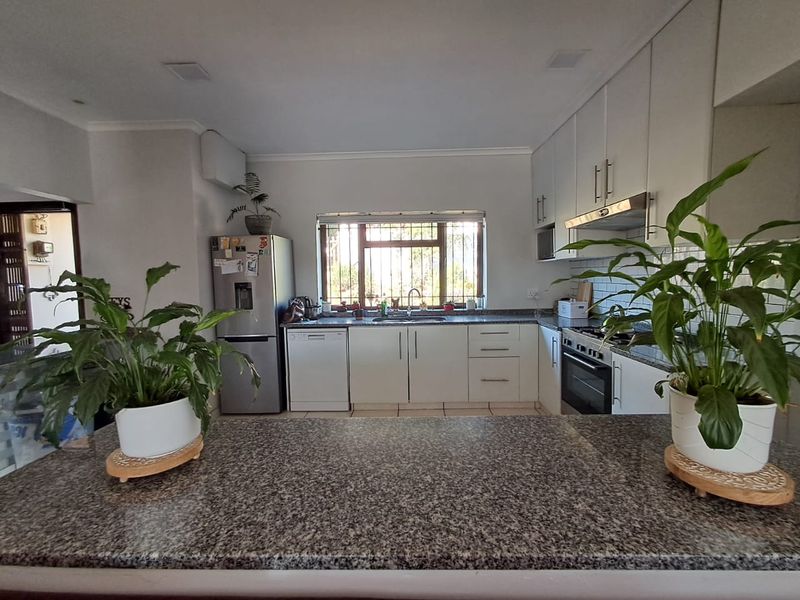 A functional kitchen featuring granite countertops, white cabinetry, a built-in oven with extractor fan, and a window with security bars.