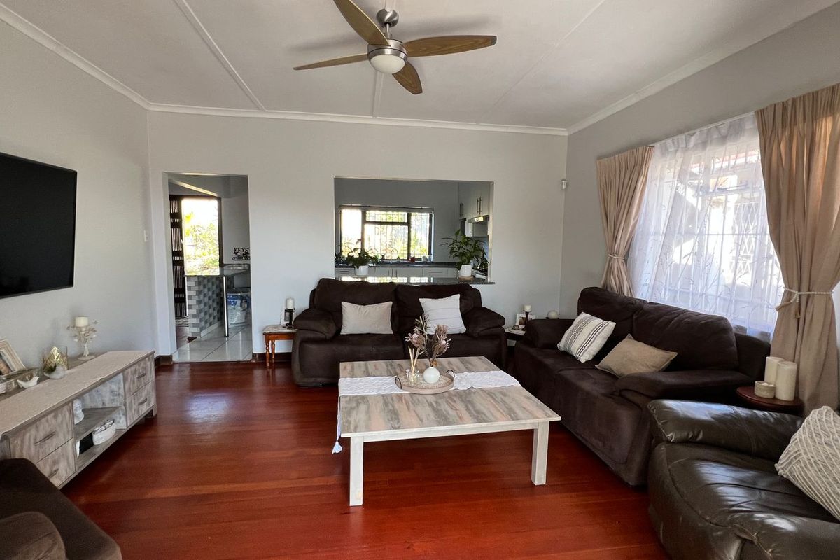 A comfortable living room featuring polished hardwood flooring, a ceiling fan, and a convenient pass-through window connecting to the kitchen area.