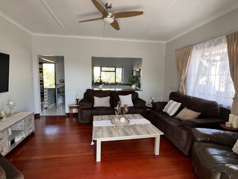 A comfortable living room featuring polished hardwood flooring, a ceiling fan, and a convenient pass-through window connecting to the kitchen area.