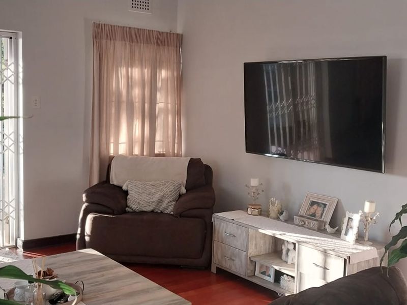 A comfortable living room featuring hardwood flooring and a sliding glass door with a security gate, providing direct access to the outdoor area.